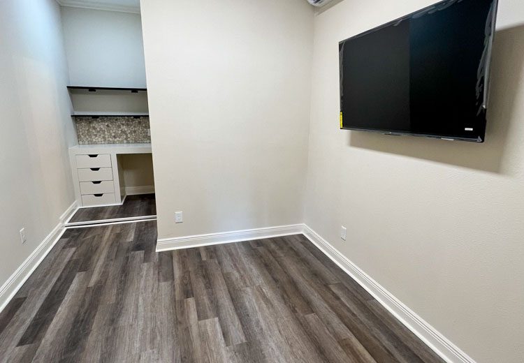 A room featuring a flat-screen TV mounted on a wall, and a bathroom